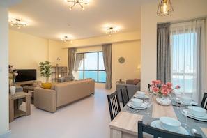 Relax in this spacious living area with a large flat-screen TV, dining table for six, and a cozy potted plant.