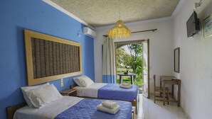 Hotelkamer met twee bedden, een klein tafeltje, een stoel, een televisie en een raam met uitzicht op groen.