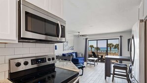 Et moderne køkken med indbygget mikroovn og komfur, et spiseområde med havudsigt og et siddeområde med en blå sofa.
