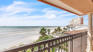 A balcony with a view of a beach, palm trees, and a hotel building.