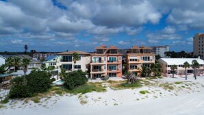 A beachfront property with multiple-story buildings, a sandy beach, and a clear sky.