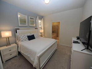 A bedroom with a bed, nightstands, a TV, and a bathroom visible through an open door. - Solterra 52 (Davenport)