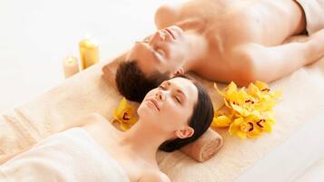 A couple lying on a massage table with towels and flowers.