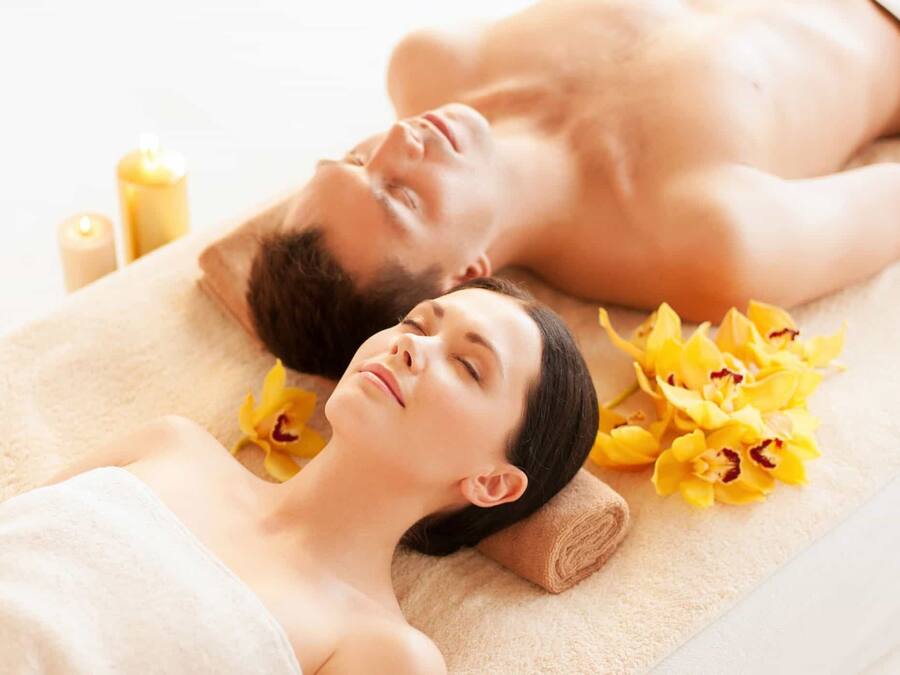 A couple lying on a massage table with towels and flowers.