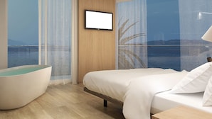 Una habitación de hotel moderna con una cama grande, una zona de estar con vista al mar y un televisor montado.