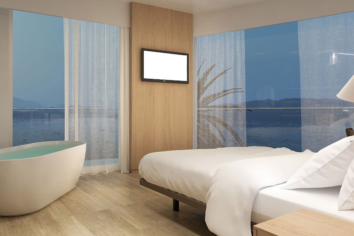 Une chambre d’hôtel moderne dotée d’un grand lit, d’un coin salon avec vue sur la mer et d’un téléviseur fixé au mur.