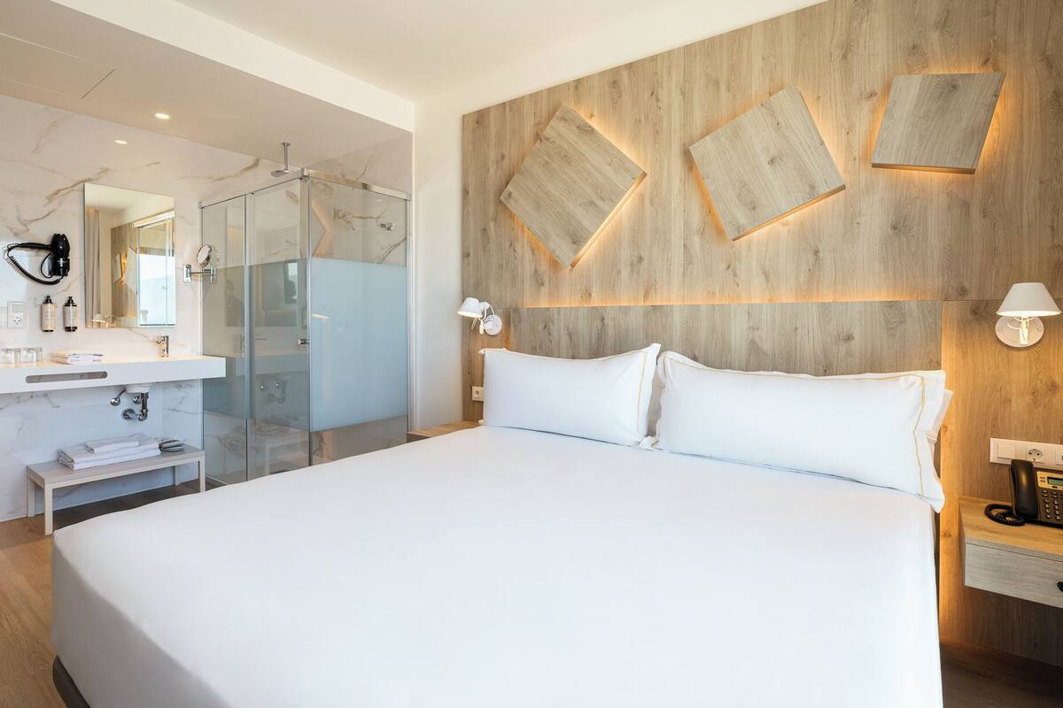 Une chambre d’hôtel moderne dotée d’un grand lit, d’une douche en verre, d’un mur d’accent en bois et d’un téléphone sur la table de chevet.