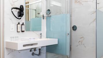 Un baño moderno con cabina de ducha de vidrio, lavamanos de mármol blanco y secador de pelo montado en la pared.