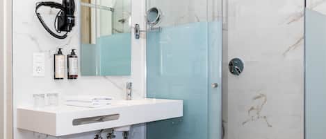 Ein modernes Badezimmer mit Duschkabine aus Glas, Waschbecken aus weißem Marmor und einem an der Wand befestigten Föhn.