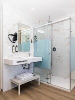 Un baño moderno con cabina de ducha de vidrio, lavamanos de mármol blanco y secador de pelo montado en la pared.