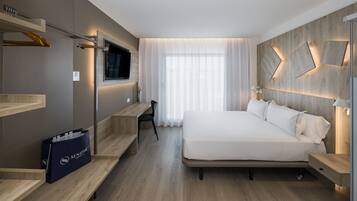 Una habitación de hotel moderna con una cama grande, un televisor montado en la pared, un escritorio con una silla y una mesita de noche de madera.