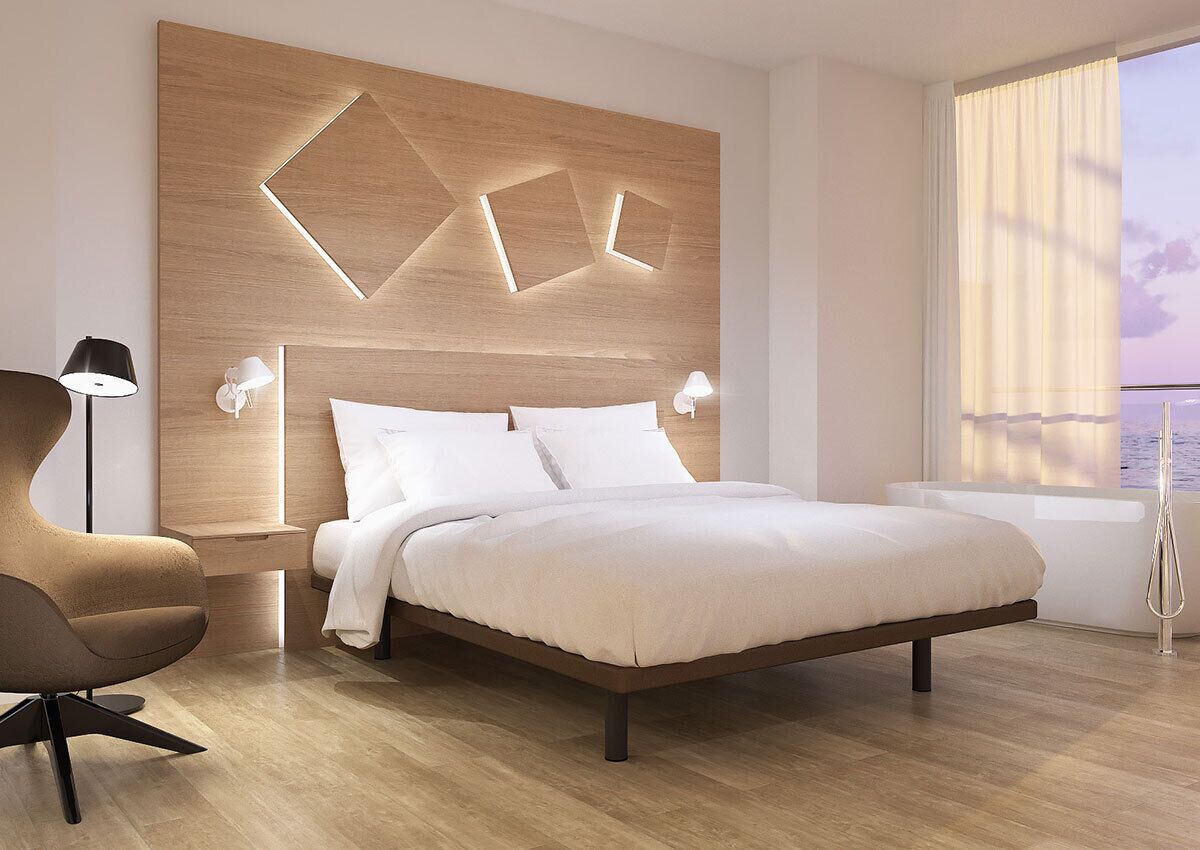 Un dormitorio moderno con cabecera de madera, una cama grande, lámparas de noche, una silla y vistas al mar a través de una ventana.