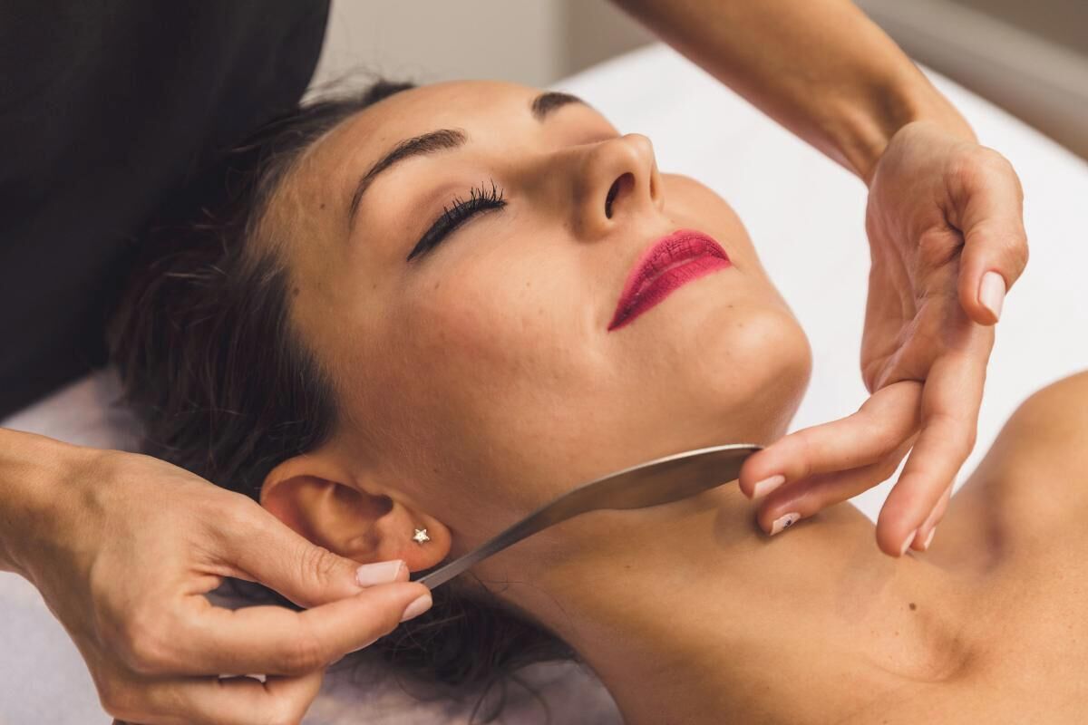 A person lying down with another person performing a procedure on their neck.