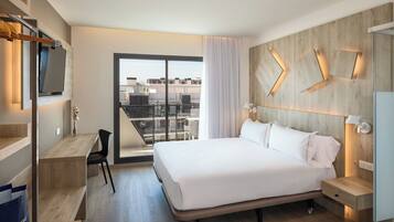 Habitación de hotel moderna con una cama grande, un escritorio, una silla y vistas a la ciudad a través de un amplio ventanal.
