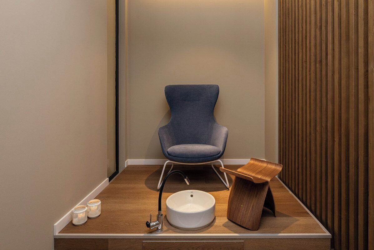 A modern bathroom with a blue chair, a wooden vanity, a white sink, and two lit candles.