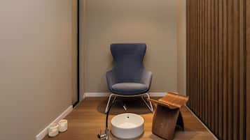 A modern bathroom with a blue chair, a wooden vanity, a white sink, and two lit candles.