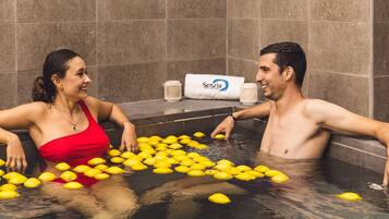 Una pareja en una bañera llena de limones, con una toalla y una taza a un lado.