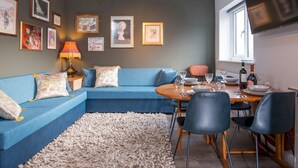 Ein modernes Wohnzimmer mit einem blauen Modulsessel, einem runden Esstisch und einem flachbildfernseher an der Wand.