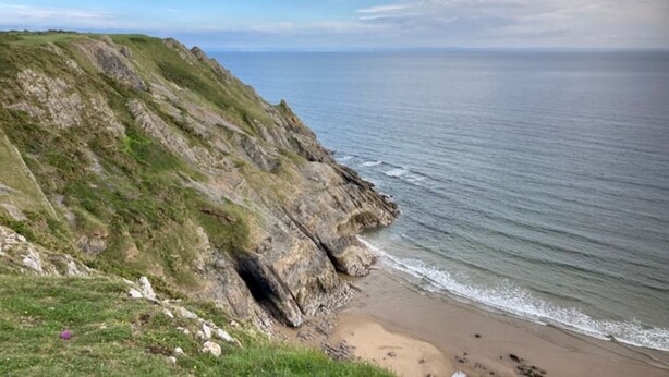 Eine Küstenlandschaft mit einer grasbewachsenen Klippe und einem Sandstrand.