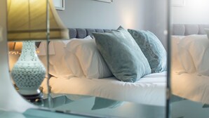 Ein modernes Schlafzimmer mit Glastisch, weißer Bettwäsche und einer Lampe.
