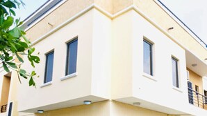 Uma casa moderna de dois andares com telhado plano, janelas amplas e uma varanda.