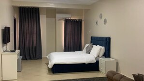 Quarto com cama, mesas de cabeceira, televisão, sofá e tapete estampado.