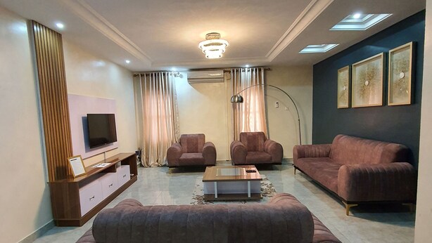 Uma sala de estar moderna com um sofá grande, duas poltronas, uma mesa de centro e uma TV sobre um console de madeira.