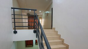 Escada com corrimão preto e degraus bege, levando a um andar superior com cortina vermelha.