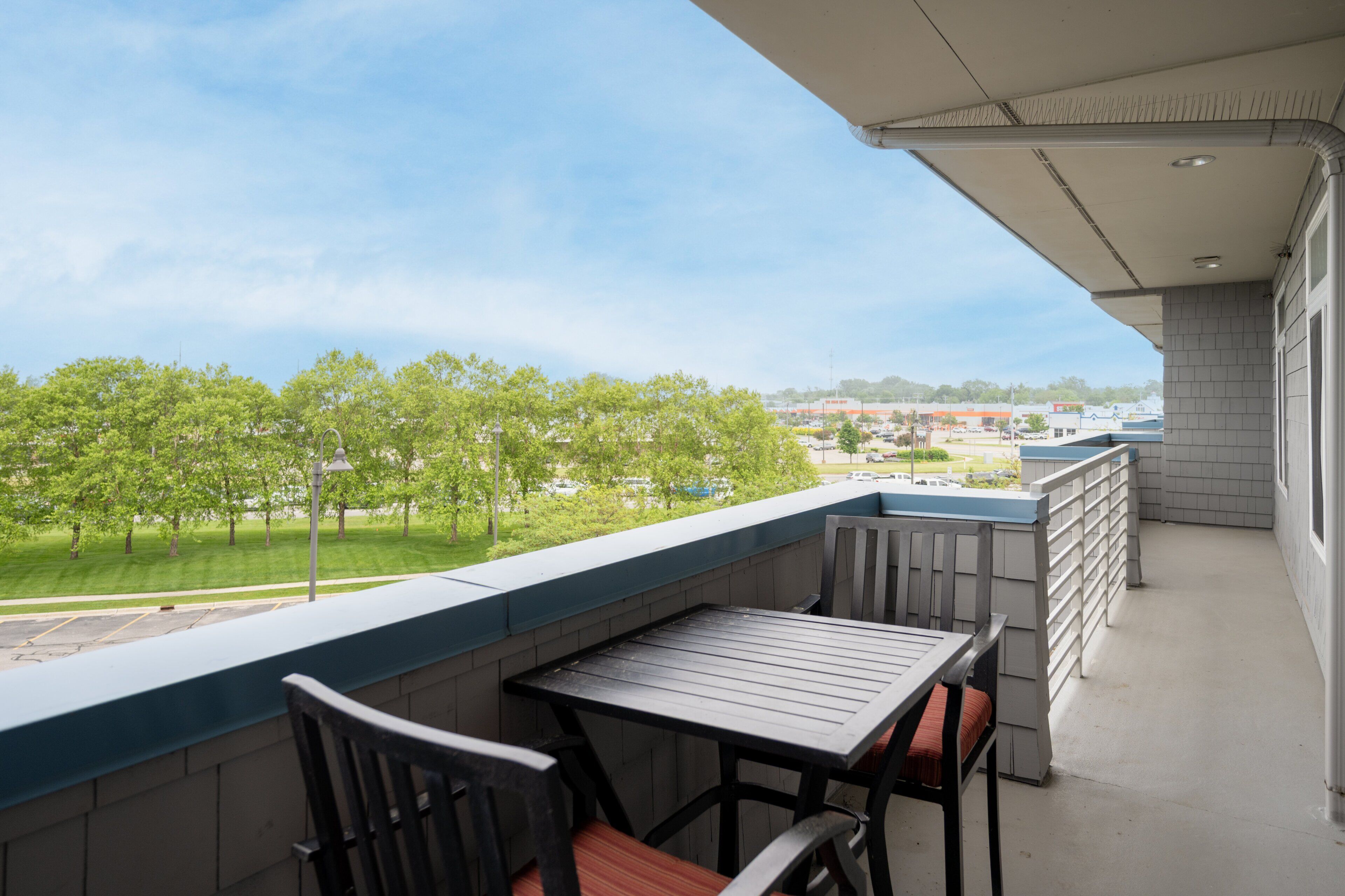 En balkon med et bord og stole, udsigt over et grønt landskab, og en bygning i baggrunden.
