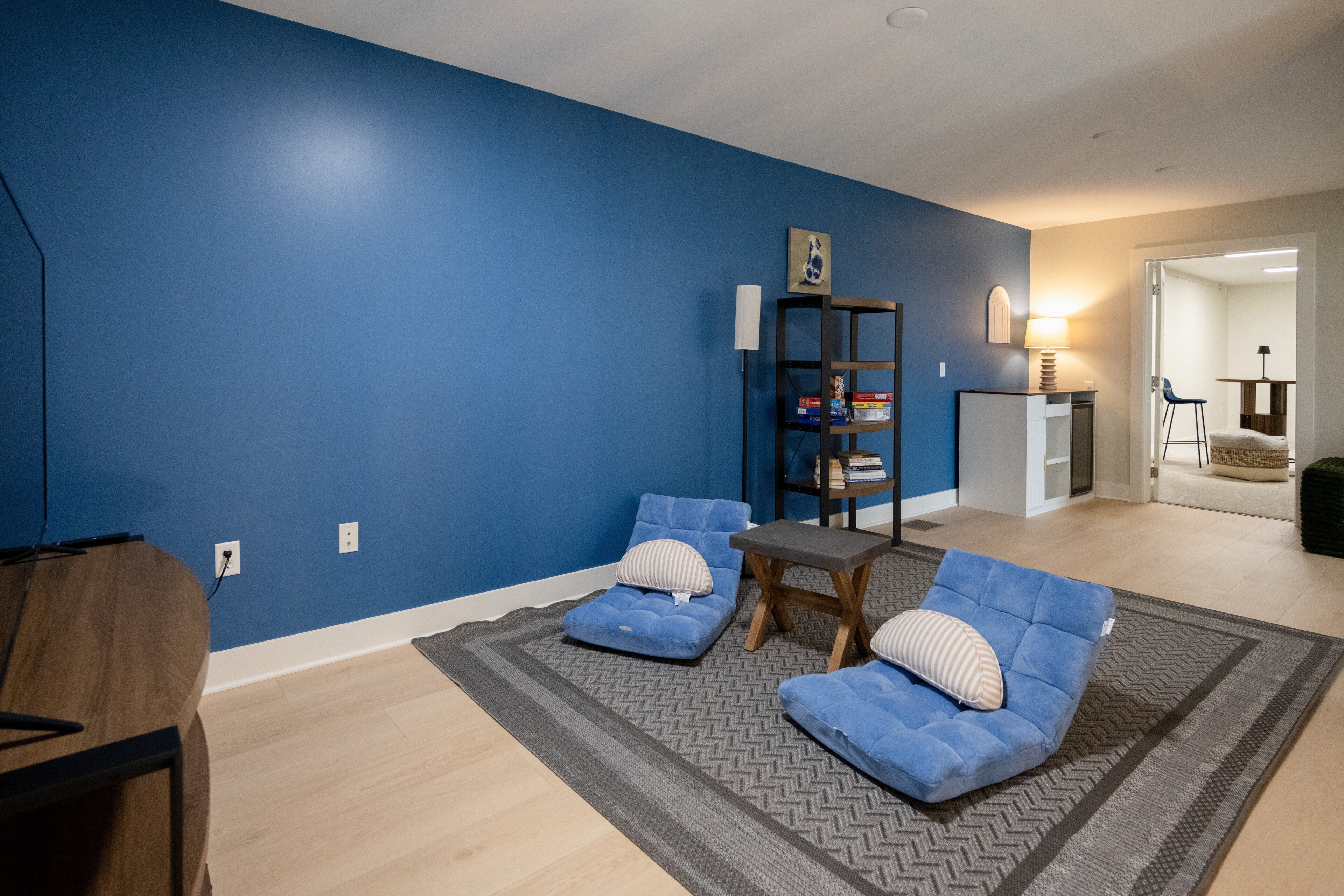A living room with blue walls, a wooden table, two blue sofas, and a grey rug.