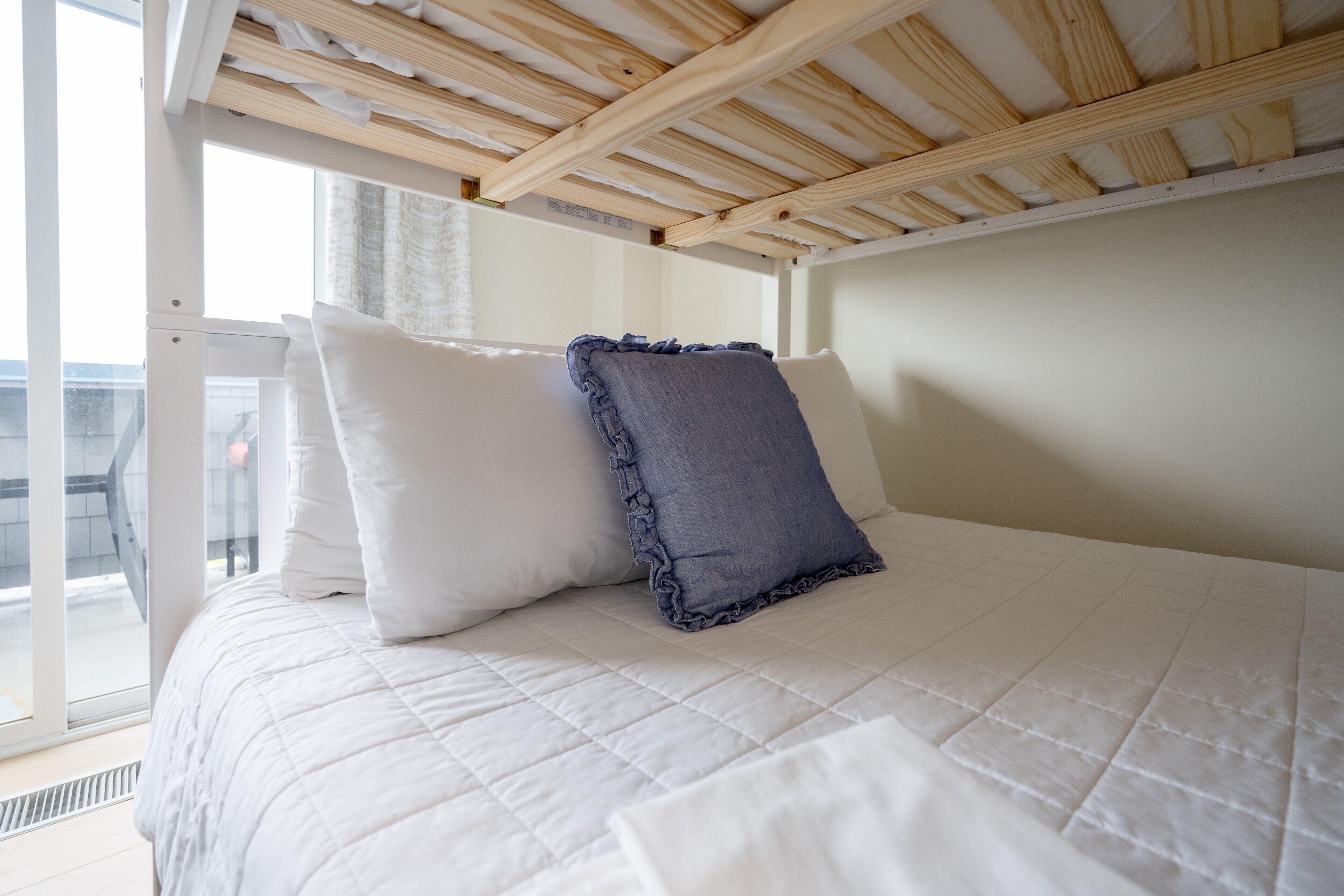 A bed with a white quilted bedspread, two pillows, and a wooden ceiling structure.