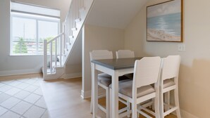 A dining area with a table and chairs, a staircase, a painting, and a large window. - Grand Haven Family Retreat | Game Loft • Sleeps 10 (Grand Haven)