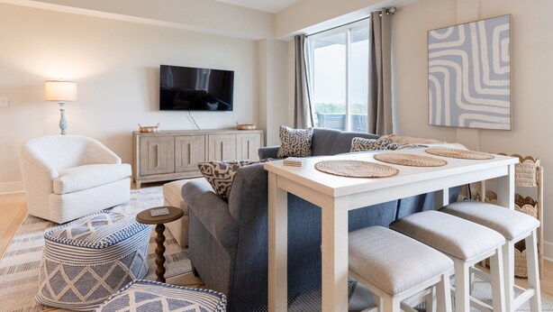 A living room with a sofa, ottoman, and a table with stools. - Grand Haven Family Retreat | Game Loft • Sleeps 10 (Grand Haven)