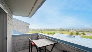 A balcony with a table and chairs, a view of a green landscape, and a building with a blue roof. - Grand Haven Family Retreat | Game Loft • Sleeps 10 (Grand Haven)