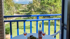 A round table with a bottle of wine, two glasses, and a plate of fruit on a balcony with a blue railing.