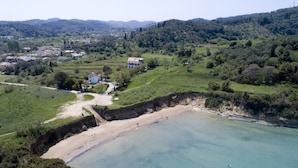 An aerial view of a coastal area with a beach, a path leading to a house, and surrounding greenery.