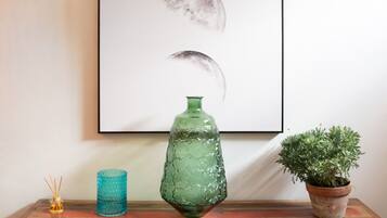Une œuvre d’art représentant les différentes phases de la lune, fixée au mur, un vase en verre vert et une plante en pot, le tout posé sur une commode en bois dotée de tiroirs.