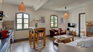 En moderne stue med sofa, spisebord med stole, et køkkenområde og et fjernsyn.