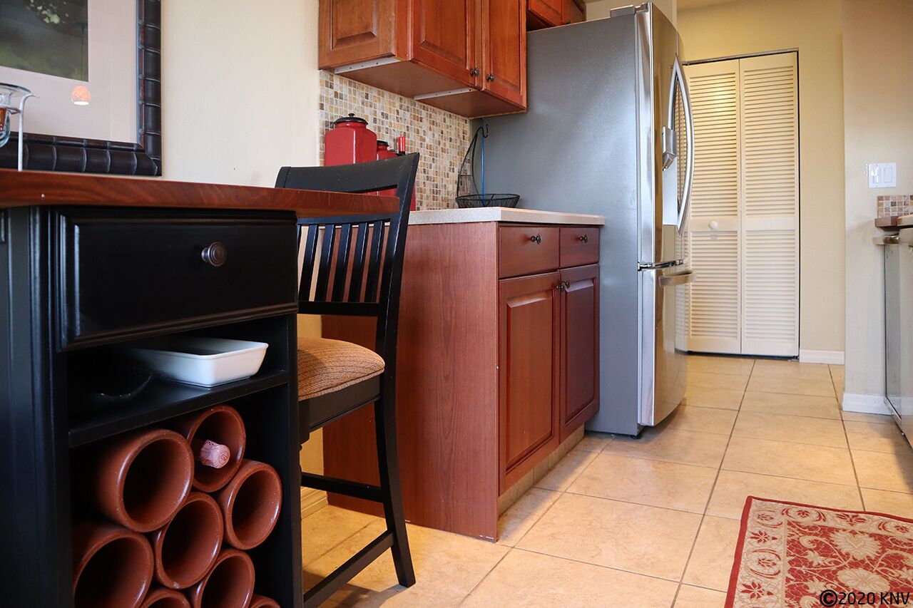 A kitchen with wooden cabinets, a black chair, a white countertop, and a tiled floor.