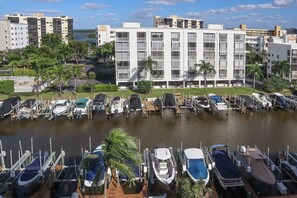A marina with multiple boats docked, surrounded by a building with a white facade and multiple windows.