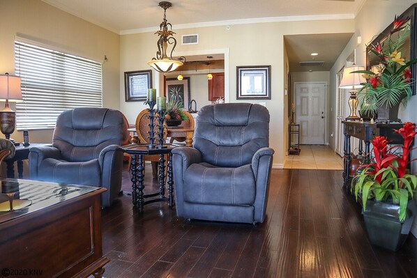 A living room with two leather armchairs, a wooden coffee table, a side table with a lamp, and a dining area with a chandelier.