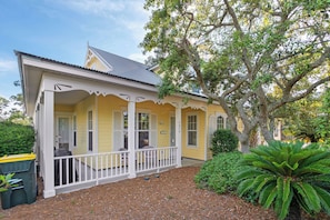 A yellow house with a porch, a tree, and a fern.