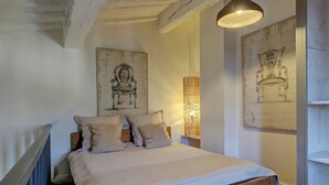 A bedroom with a wooden bed, two pillows, a hanging light fixture, and two wall-mounted artworks.