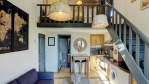 A spacious living area with a high ceiling, a staircase, a kitchen, and a dining area.