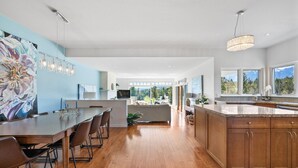 Una cocina moderna con suelo de madera, un comedor con una mesa grande y vistas a un paisaje montañoso a través de amplios ventanales.