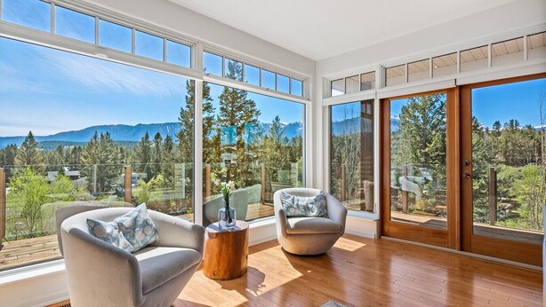 Un salón comedor amplio con ventanas grandes que ofrecen vistas a la montaña, dos sillones cómodos y una mesa de centro de madera.