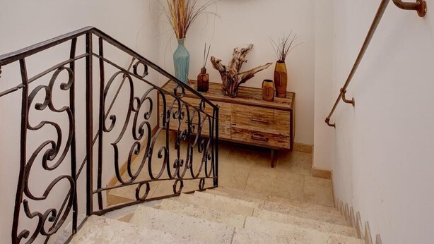 Una escalera con barandilla de hierro forjado, un banco de madera y dos lámparas de mimbre.