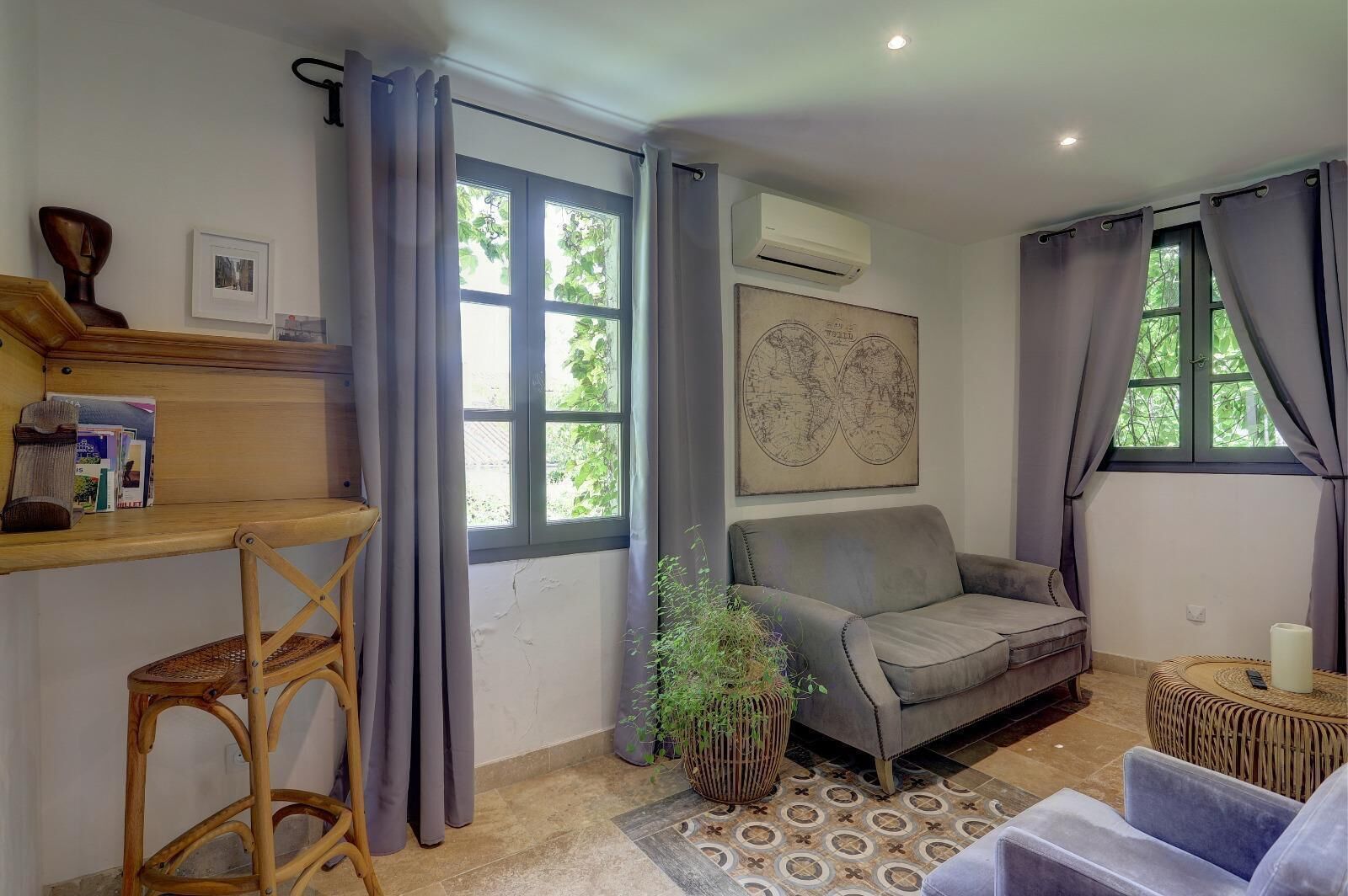 A cozy living room with a grey sofa, a wooden side table, a small stool, a potted plant, and a world map on the wall.