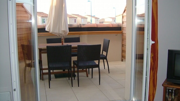 En balkon med et bord og stole, en skydedør og et fjernsyn på et stativ.