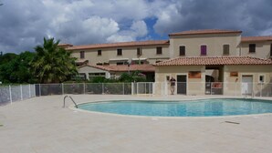 En udendørs swimmingpool med fliseterrasse, omgivet af et hvidt hegn og palmer.